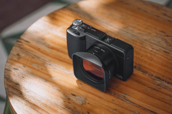 Ricoh GR IV med fyrkantigt JetMag Pro-motljusskydd på ett runt träbord