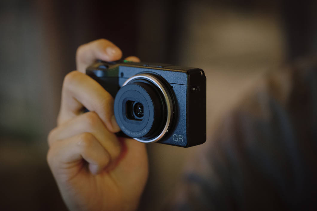 Ricoh GR IV med en blå NiSi-ring runt objektivet hålls upp mot ögat